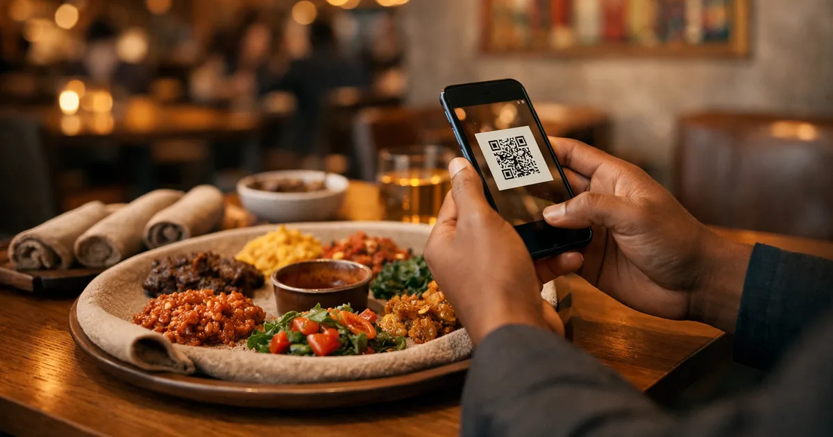 A restaurant guest in a modern upscale Addis Ababa restaurant holds a smartphone scanning a QR code menu, with traditional injera bread and colourful spiced wot dishes on a wooden table, warm amber pendant lighting